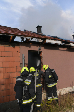 három tűzoltó az ajtónyíláson át locsol be az épületbe